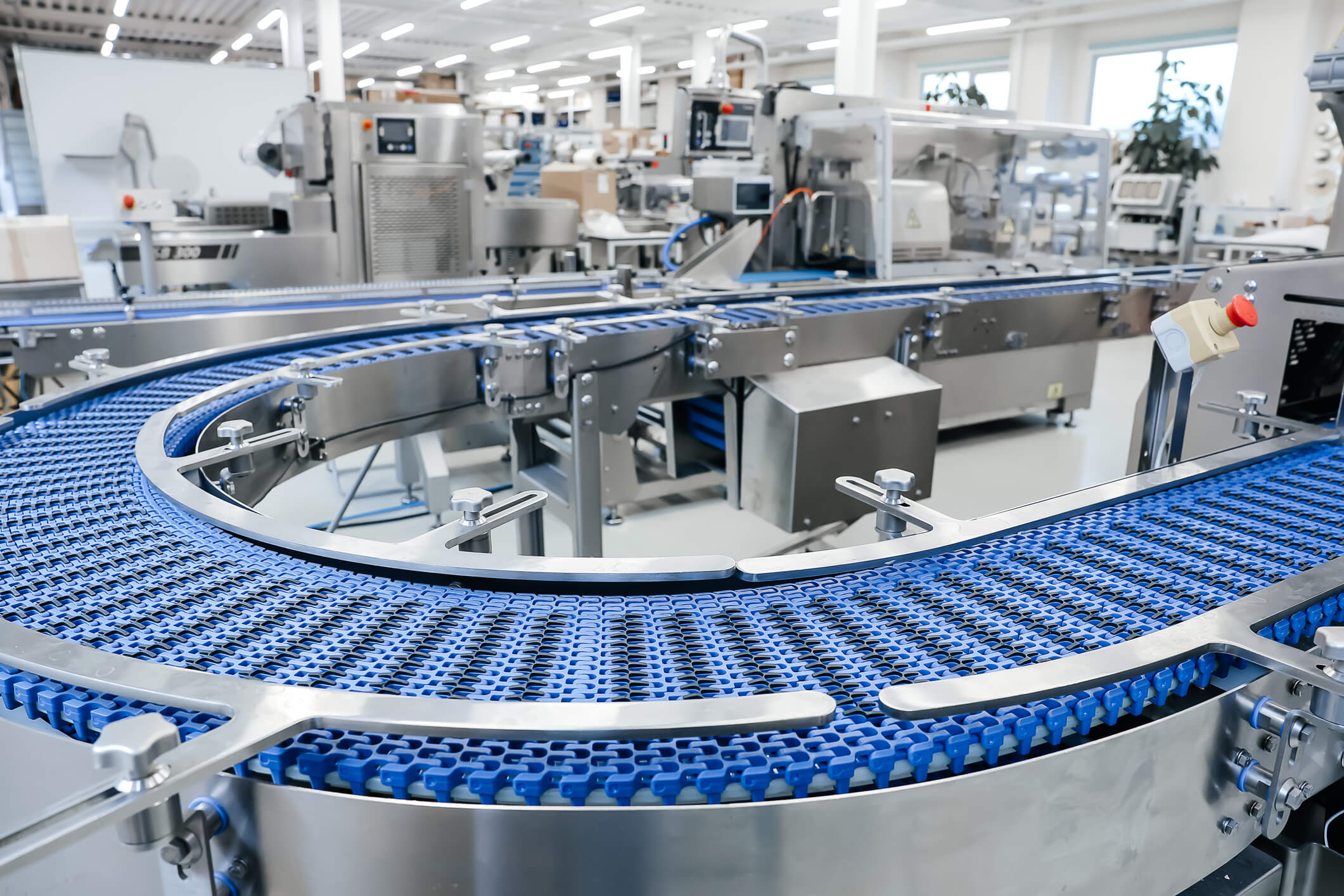 Curved blue conveyor belt running through an automated packaging and production line.