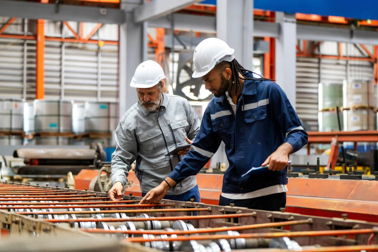 Two engineers in hard hats inspecting metal components on a production line.