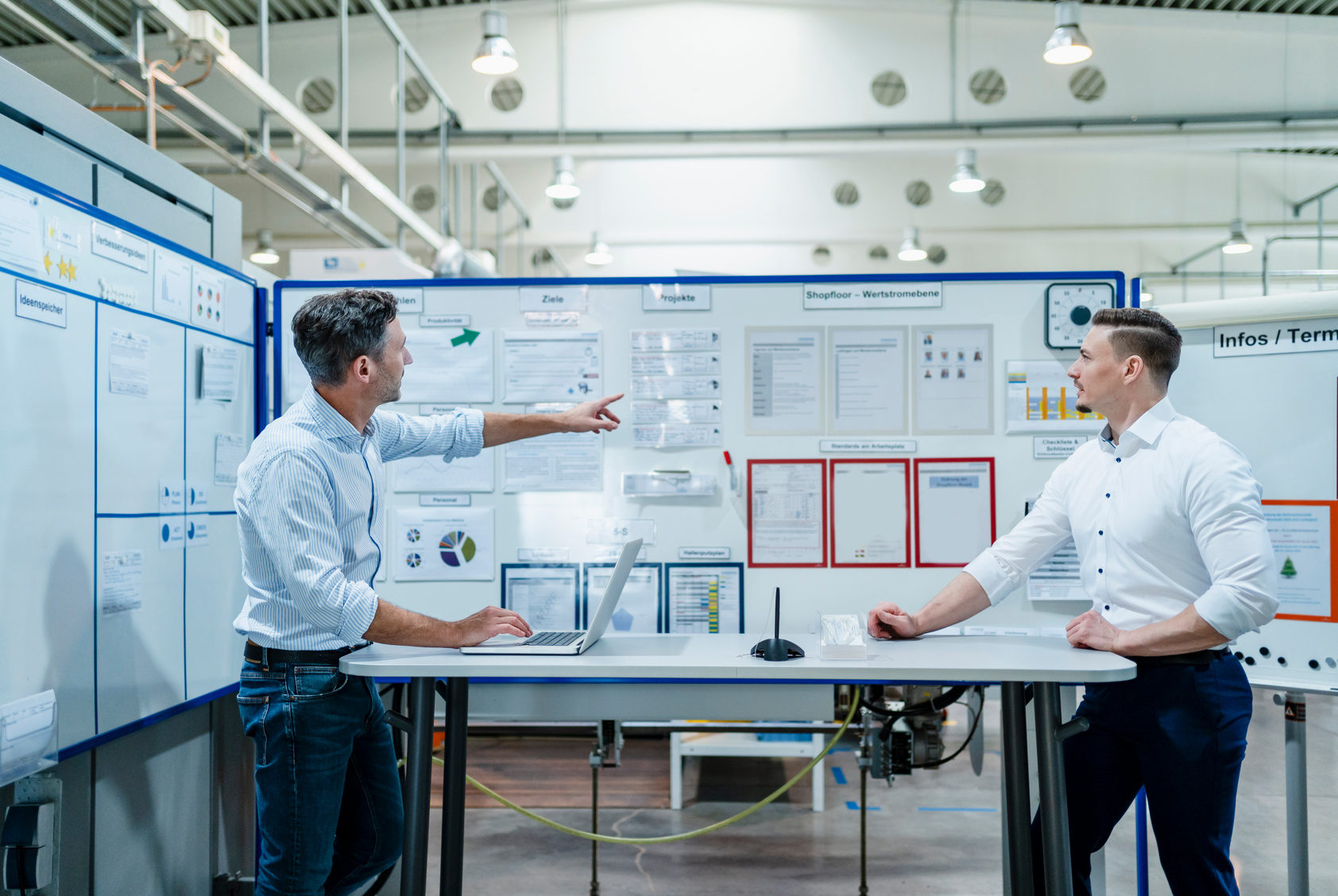 Two business colleagues discussing performance charts at a visual management board in an industrial facility.