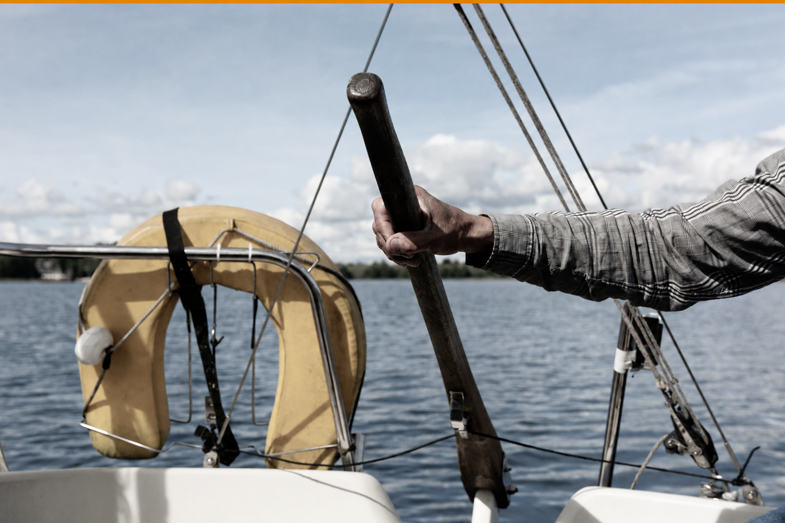 Hand gripping a winch handle on a sailing boat, with a lifebuoy and open water behind.