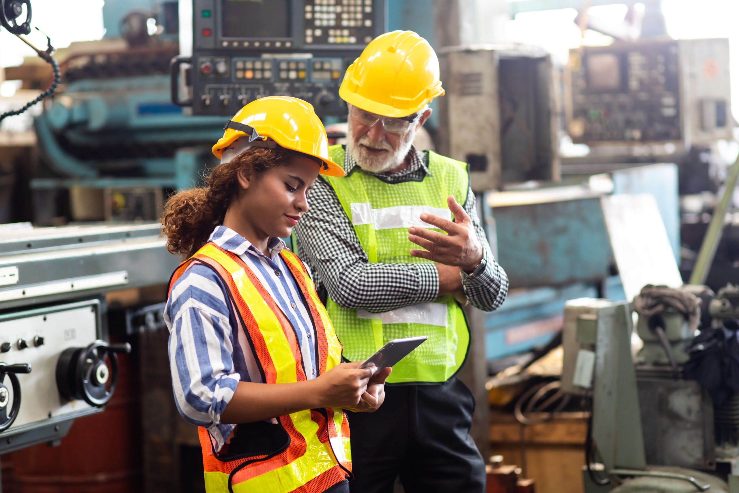Experienced manufacturing colleague coaching a team member beside production equipment.