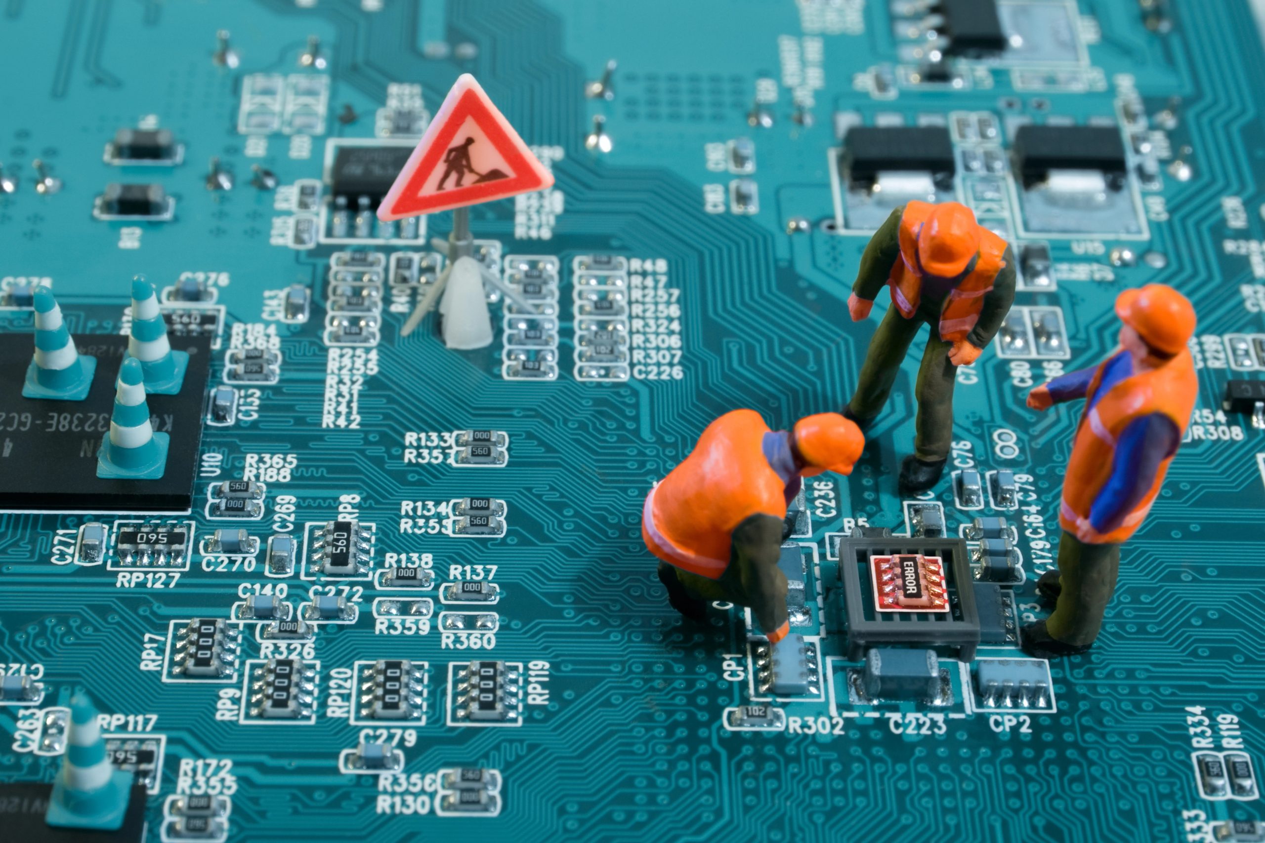 Depositphotos_7906156_XL Miniature workers in hi-vis clothing repairing a circuit board beside a roadworks warning sign.